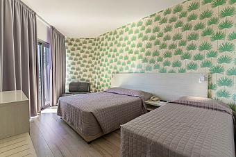 Hotelzimmer mit zwei Doppelbetten, grüner gemusterter Tapete und Sessel