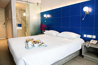 Gemütliches Zimmer mit Doppelbett, blauer Wand und Frühstückstablett neben dem Eingang zum Marmorbadezimmer