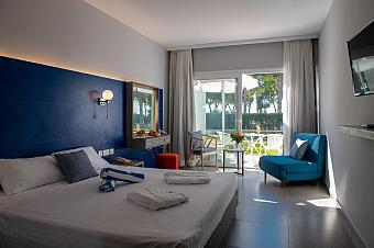 Modernes Hotelzimmer mit blauer Akzentwand, weißer Bettwäsche und Blick auf die Terrasse