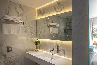 Elegantes Marmorbad mit beleuchtetem Spiegel, weißem Waschbecken und ordentlich gefalteten Handtüchern auf Regalen