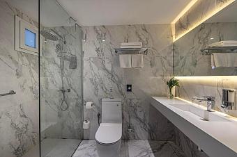 Geräumiges Marmorbad mit Glasdusche, Toilette, langer Ablagefläche und stimmungsvoller Beleuchtung