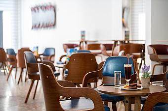 Modernes Hotelcafé mit Holzstühlen, kleinen Tischen und einem Getränk, serviert mit Snacks und Blumen