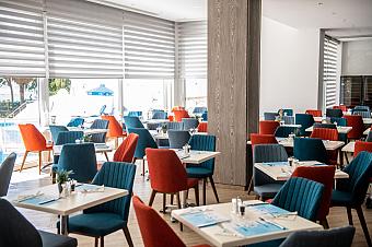 Moderner Innenbereich des Restaurants mit bunten blauen und orangefarbenen Stühlen um quadratische Tische angeordnet