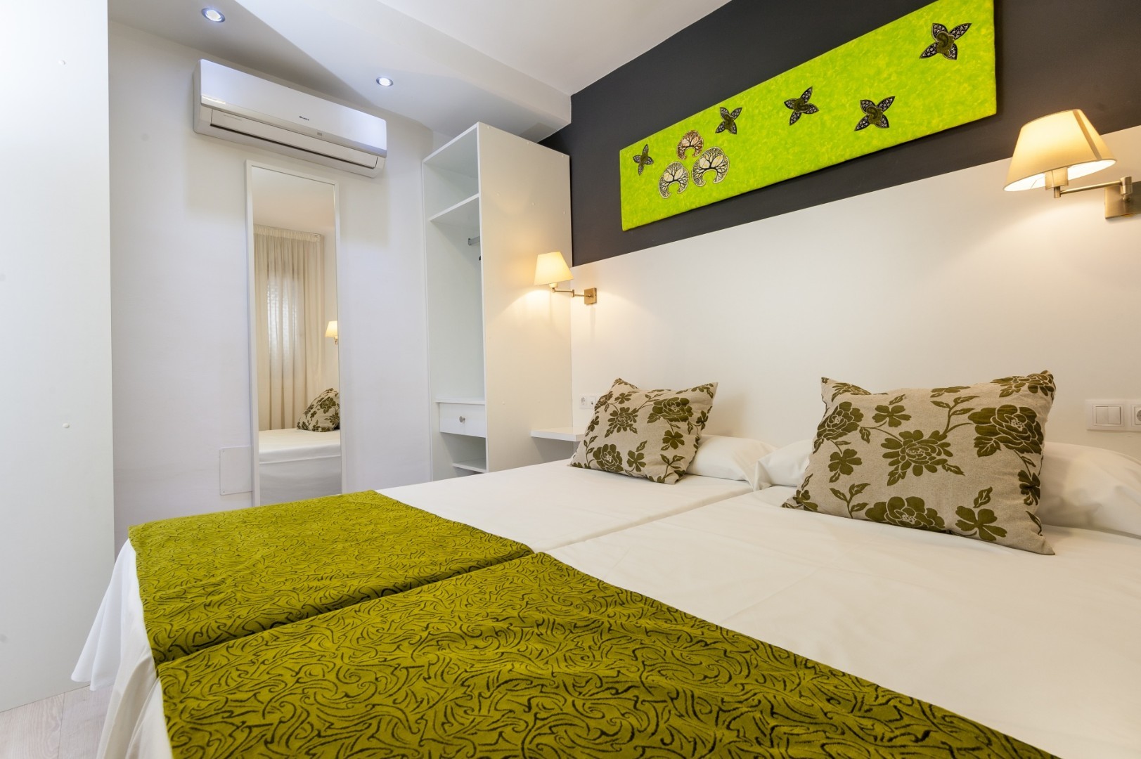 Bright bedroom with twin beds, green bedspread, and wall-mounted artwork.
