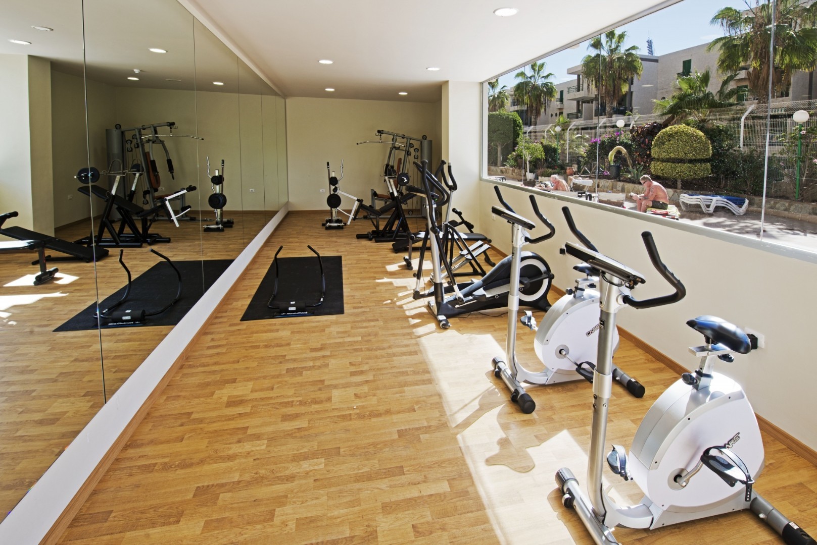 Fitness room with stationary bikes, strength machines, mirrors, and a large window.