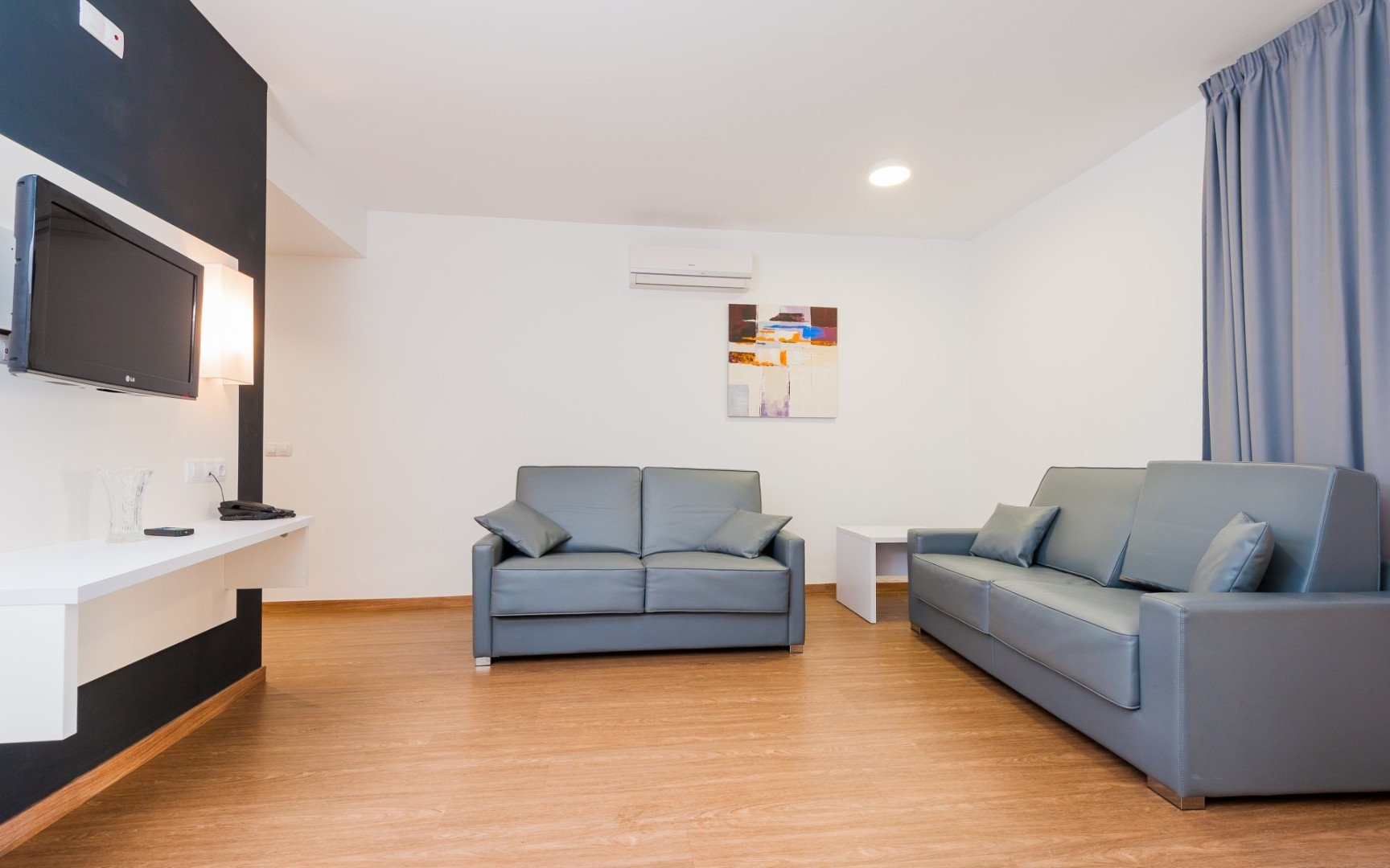Modern living room with two gray sofas, wall-mounted TV, and wood flooring.