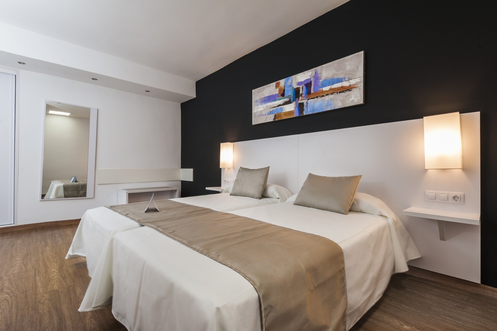 Spacious twin bedroom with black feature wall, large mirror, and wooden flooring.