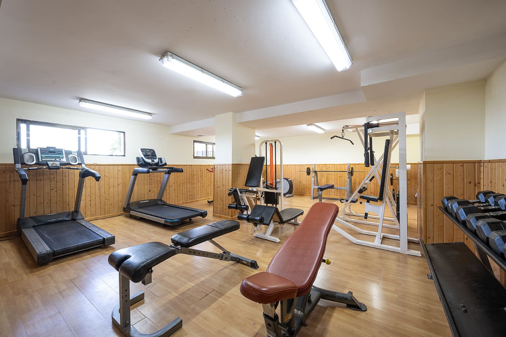 Fitnessraum mit Laufbändern, Bänken, Kraftgeräten und Hanteln für Indoor-Workouts.