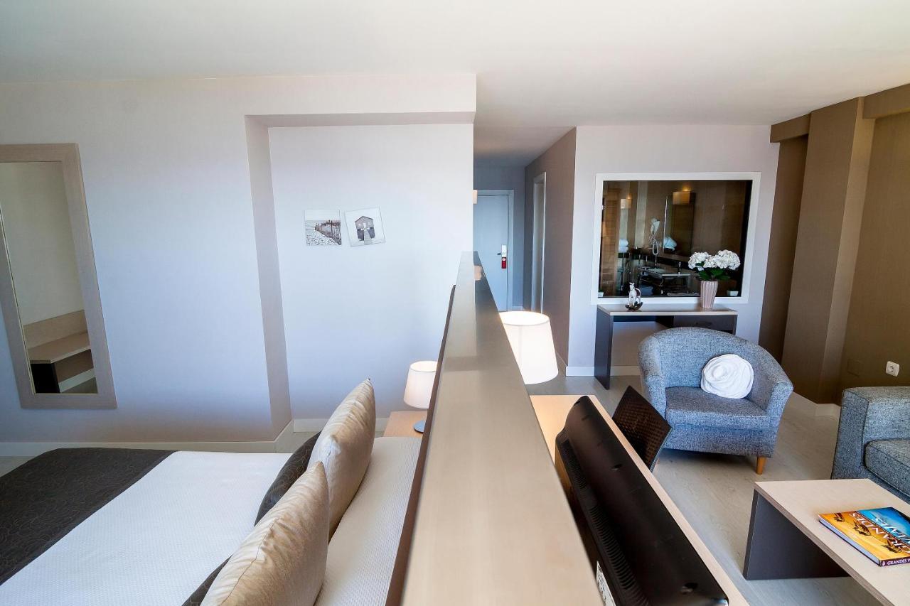 Offen geschnittenes Zimmer mit Schlafbereich, Sessel und Innenfenster zum Bad.