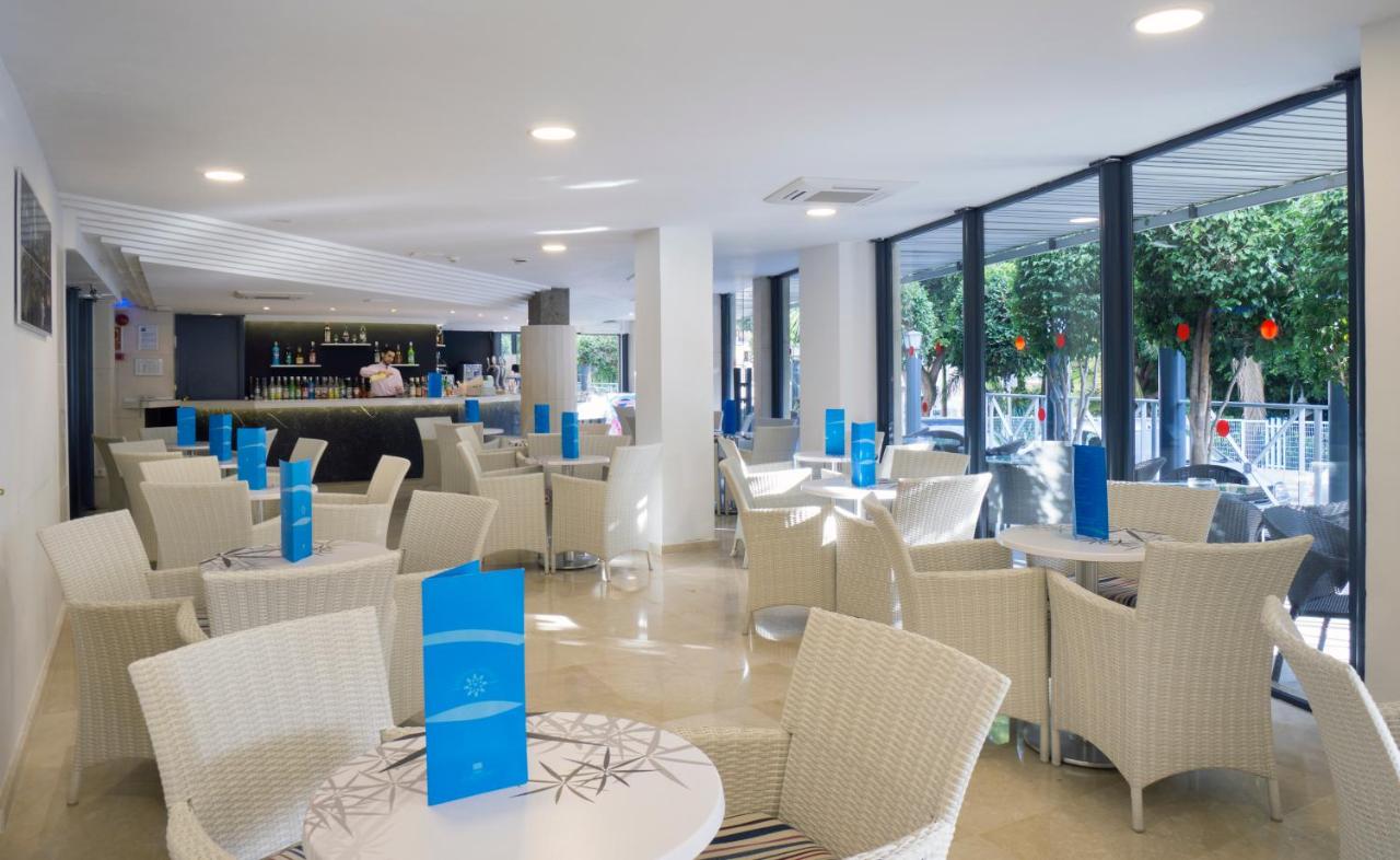 Hotelbar-Lounge mit Korbstühlen, Rundtischen und großen Fenstern.