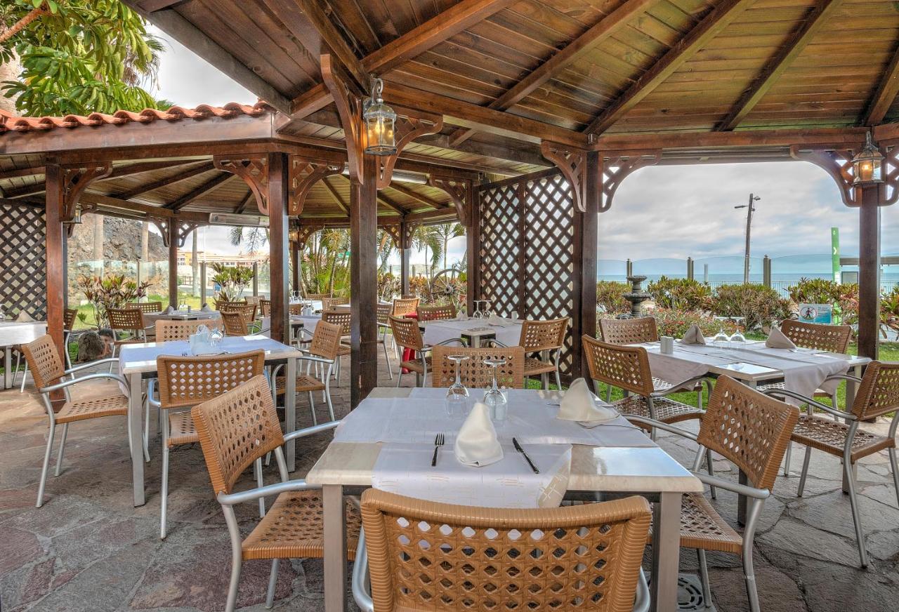Restaurant terrace with set tables under a wooden pergola near the waterfront.