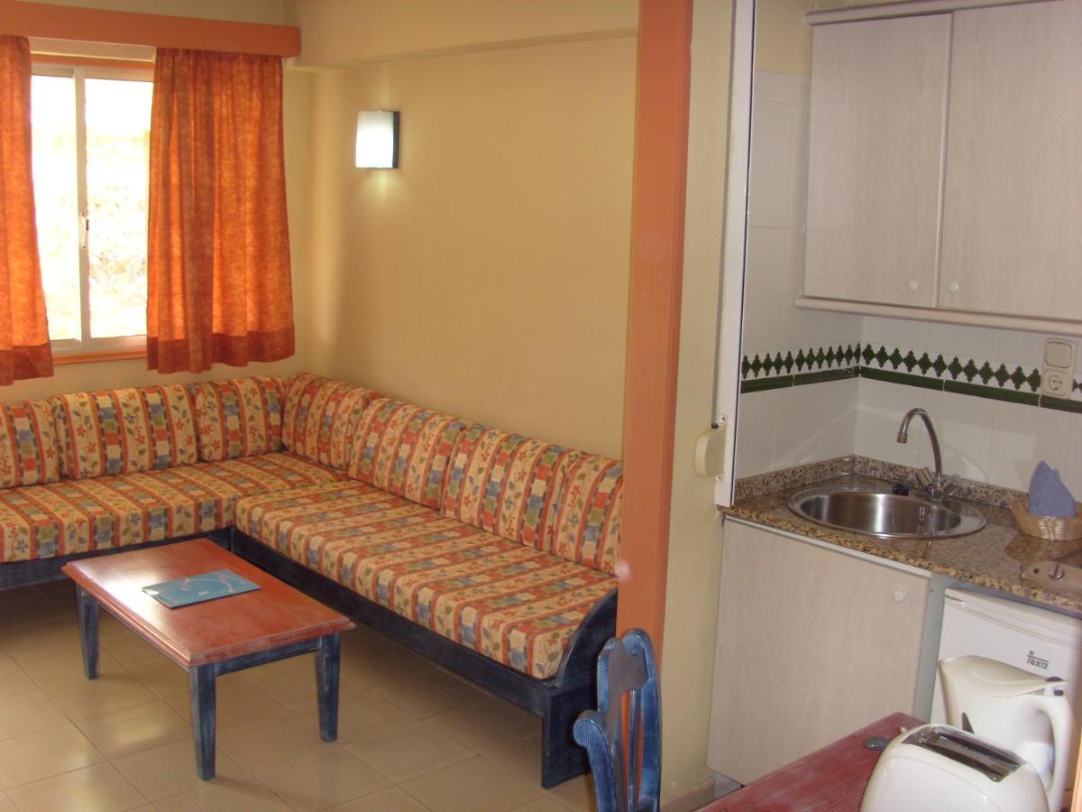 Apartment living area with corner sofa, coffee table, and kitchenette with sink.