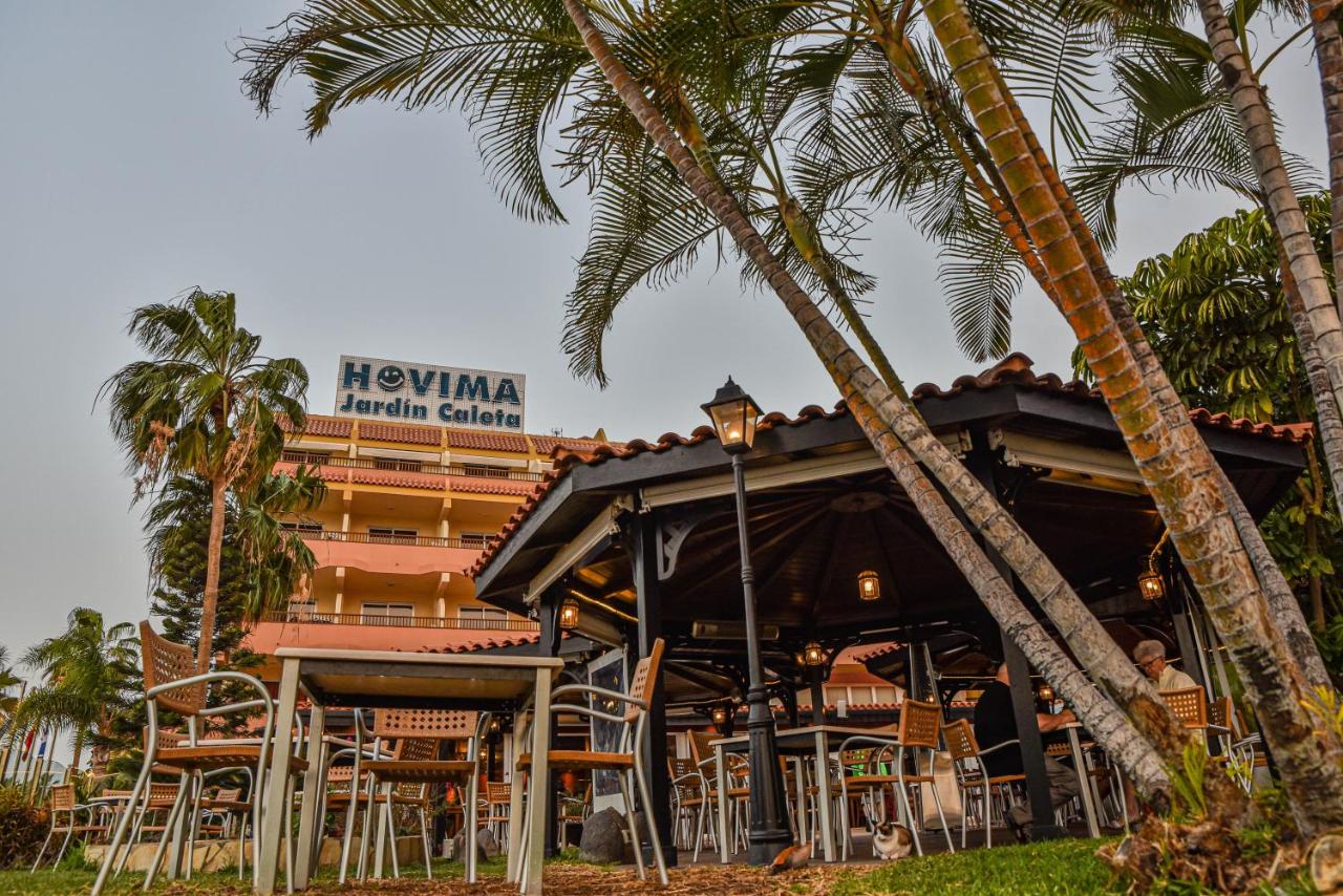 Outdoor terrace seating under a gazebo with palm trees and the hotel building behind.
