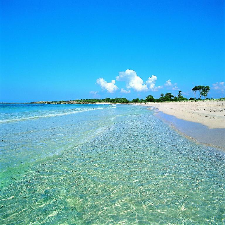 Mer peu profonde aux eaux claires et plage de sable sous un ciel bleu.