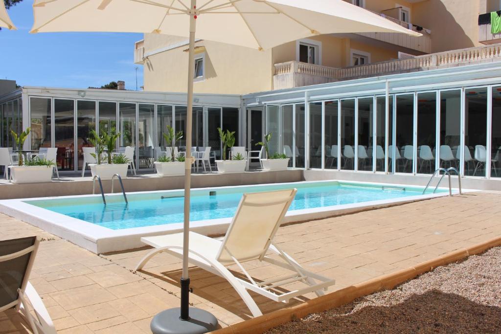 Piscine extérieure avec chaises longues et parasol à côté d'une terrasse aux parois vitrées.