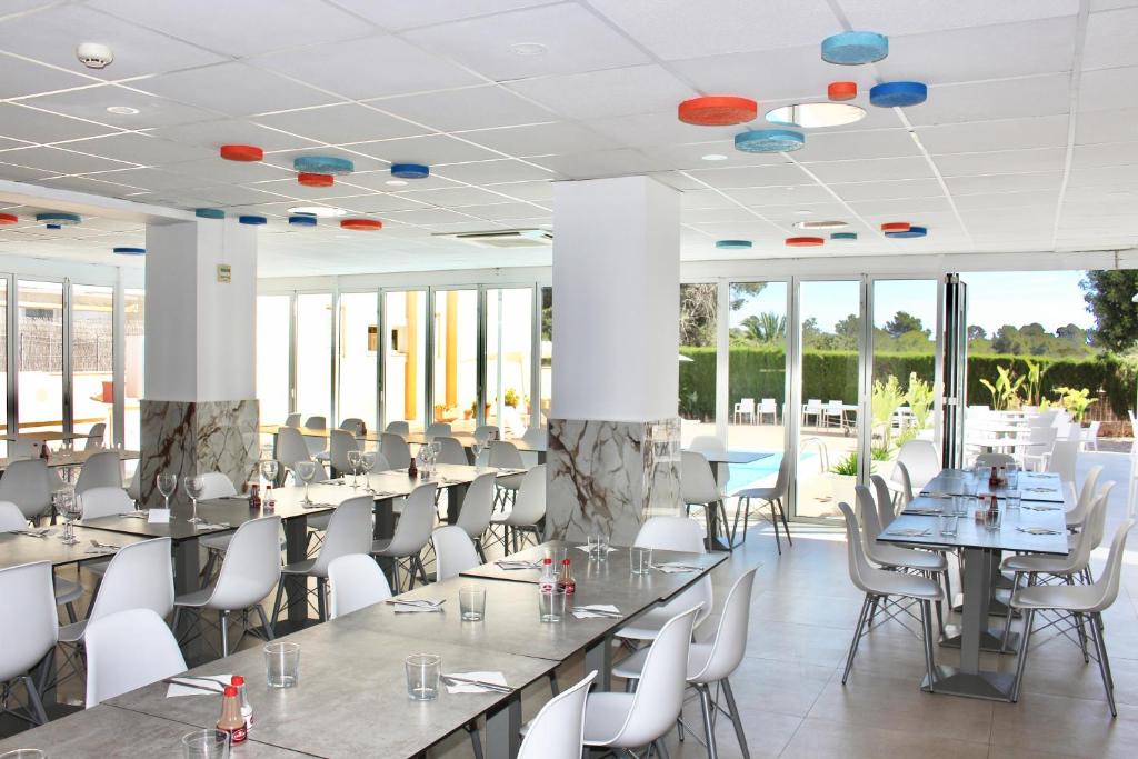 Salle à manger lumineuse avec grandes tables, chaises blanches et grandes portes coulissantes donnant sur le patio.