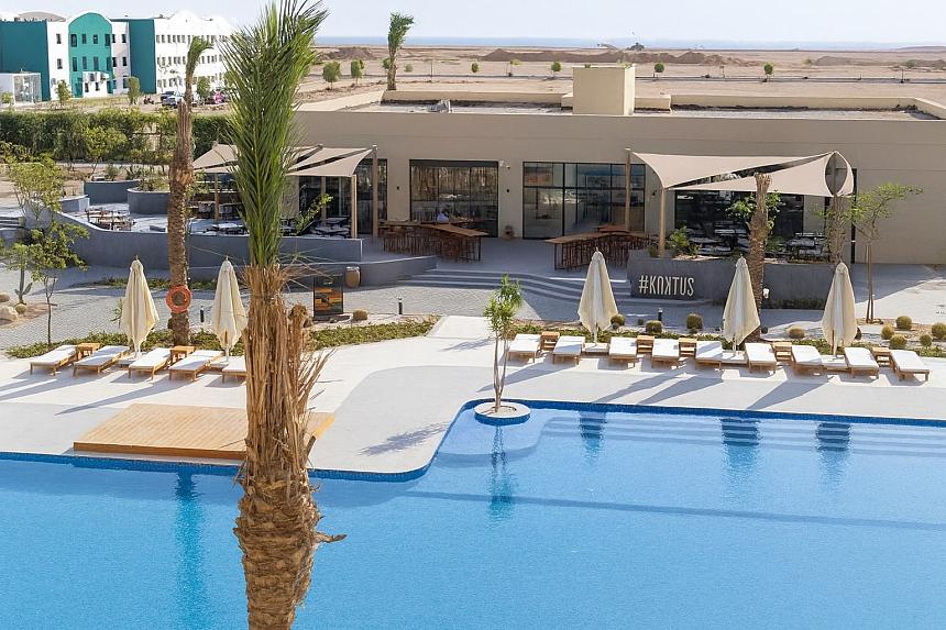 Außenpool mit Sonnenliegen, Sonnenschirmen und Palmen nahe dem Resortgebäude