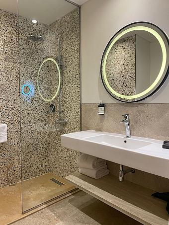 Bathroom with glass shower, round illuminated mirror, and sink