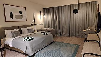 Hotel room with king bed, sofa, desk, and large window with curtains