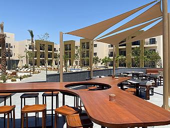 Outdoor bar area with wooden counter, stools, and shade sails near poolside