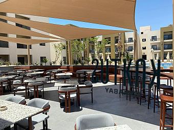 Open-air dining terrace with tables, chairs, and shade canopy by the resort