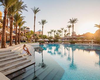 Lagoon pool with palm trees and woman relaxing on steps at sunset