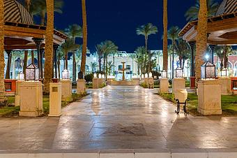 Pathway lined with palm trees and lanterns leading to resort entrance at night