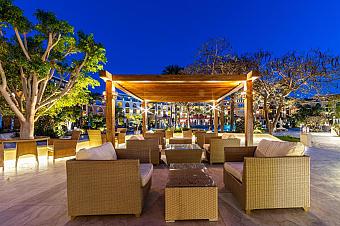 Outdoor lounge area with wicker sofas under wooden pergola at night