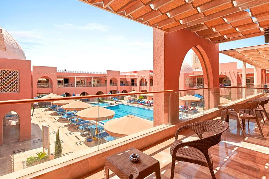 Balcony view of resort pool with umbrellas and arched red architecture