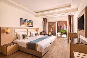 Bright hotel room with twin beds, artwork, and terrace access with outdoor seating