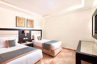 Bright hotel room with two single beds, wall art, TV, and neutral decor
