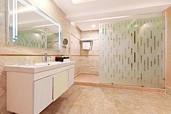 Modern hotel bathroom with large mirror, sink, and glass-enclosed shower with frosted design