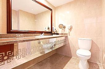 Bathroom with large mirror, sink, and toilet in beige tiles