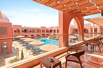 Balcony view of resort pool with umbrellas and arched red architecture