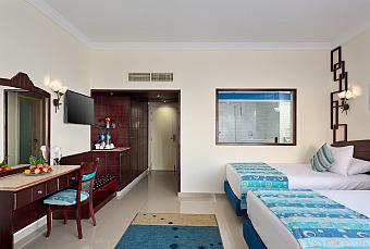 Modern twin room with blue accents, desk, TV, and partial view into bathroom, suitable for athletes’ stay during training camp