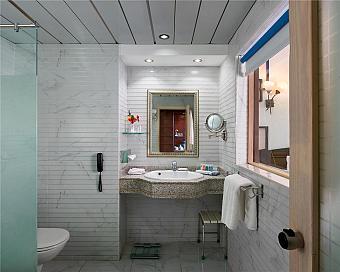 Modern hotel bathroom with marble walls, mirror, and glass shower enclosure