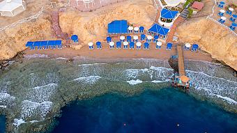 Aerial view of private beach with blue sun umbrellas, loungers, and wooden pier extending over clear water