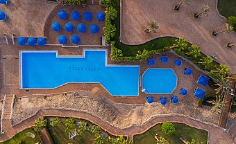Aerial view of two outdoor pools with blue umbrellas and palm trees at Club Reef Resort