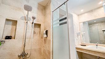 Modern beige marble bathroom with glass shower, rain showerhead, and large mirror