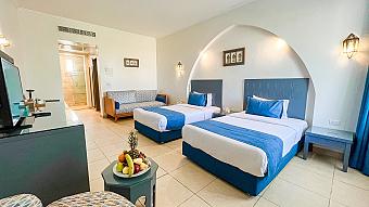 Bright hotel room with twin beds, blue decor, and sitting area, ideal for athletes during training camps