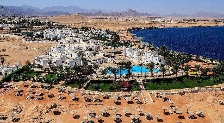 Aerial view of seaside resort with white buildings, palm trees, pools, and sunbeds overlooking the Red Sea