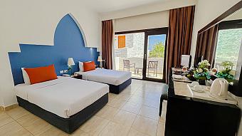 Bright twin room with blue and orange accents, private balcony, and outdoor seating overlooking the resort