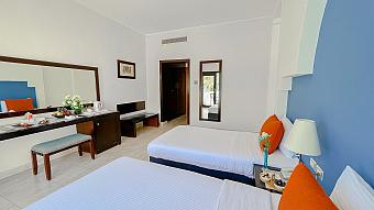 Modern hotel room with twin beds, blue accent wall, and orange pillows, featuring a work desk and fresh decor