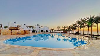 Resort pool surrounded by palm trees and white buildings at sunset