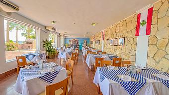 Bright dining room with blue checkered tablecloths, large windows, and stone wall decor