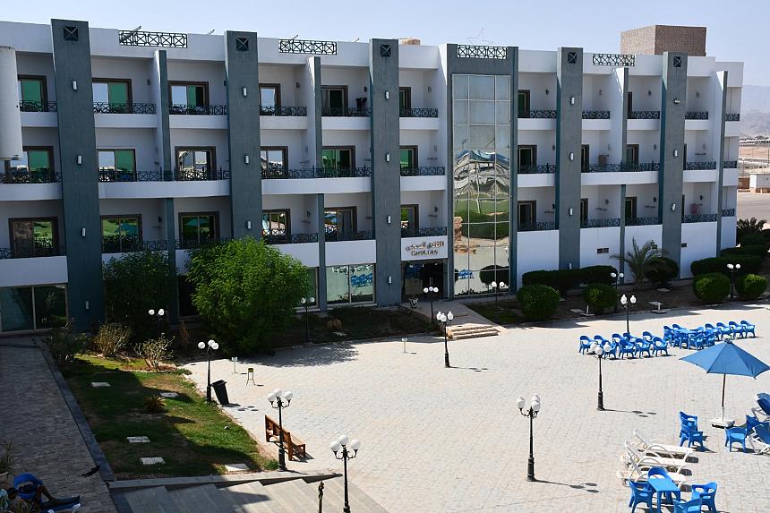 Modern three-story hotel building with balconies, glass entrance, and outdoor seating area