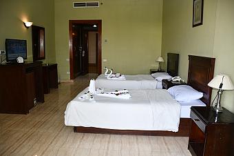 Hotel room with twin beds, light green walls, and a TV, prepared for sports camp accommodation