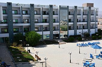 Modern three-story hotel building with balconies, glass entrance, and outdoor seating area