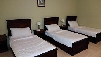 Spacious triple room with three single beds, wooden headboards, and bedside lamps