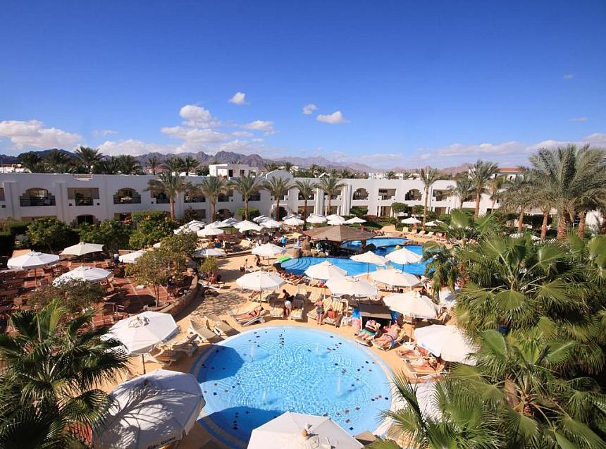 Aerial view of resort courtyard with multiple pools, palm trees, and guests sunbathing under umbrellas